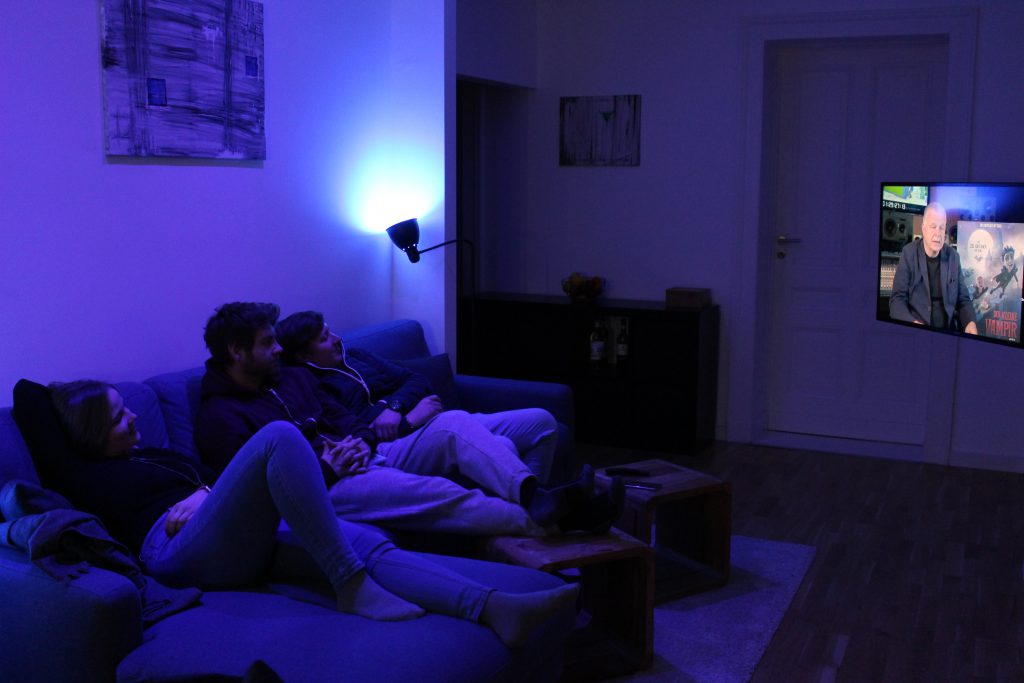 Alle Mitbewohner sitzen auf der Couch, das Licht leuchtet blau.